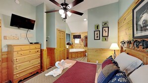 A bedroom with a bed, wooden dresser, television, ceiling fan, and artwork on the walls. - Americana by Jackson Mountain Rentals (Gatlinburg)