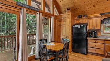 A wooden cabin with a dining table, chairs, and a kitchen area.