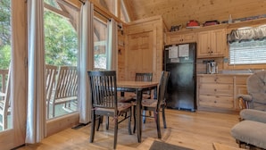 A wooden cabin interior with a dining table and chairs, a kitchen area with a refrigerator, and large windows with curtains. - Americana by Jackson Mountain Rentals (Gatlinburg)