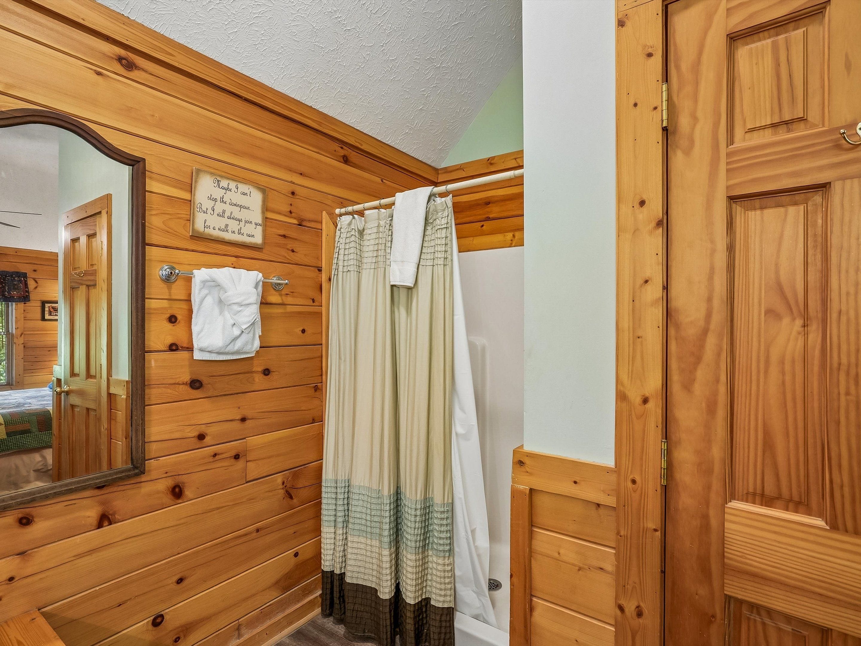 A wooden bathroom with a shower curtain, a towel hanging on the wall, and a mirror.