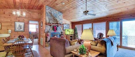 A cozy cabin interior with a dining area, a fireplace, and a large window.