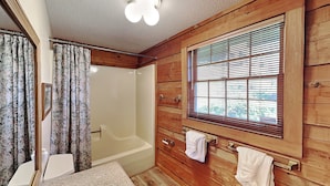 A wooden cabin bathroom with a bathtub, a sink, and a window with blinds. - Alpine Windsong by Jackson Mountain Rentals (Gatlinburg)