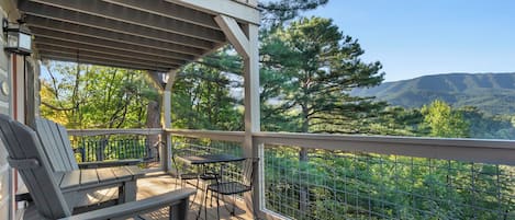 A wooden deck with outdoor furniture, a pergola, and a view of a forested mountain range.