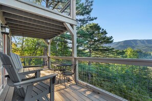 A wooden deck with outdoor furniture, a pergola, and a view of a forested mountain range.