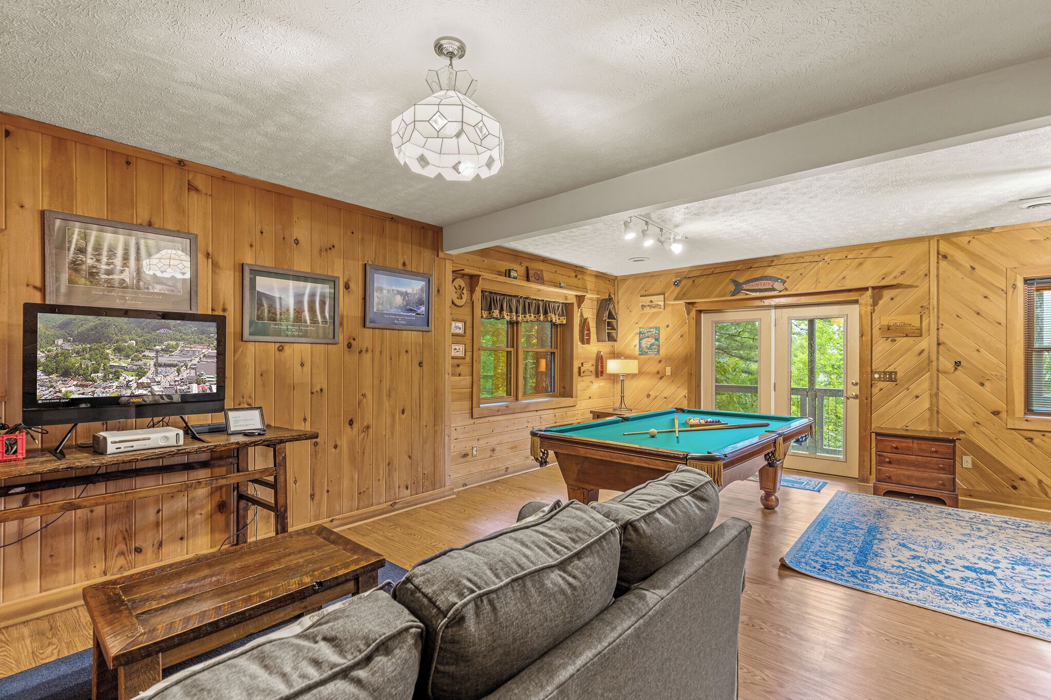 A wooden-paneled room with a pool table, a sofa, a television, and framed pictures on the wall.