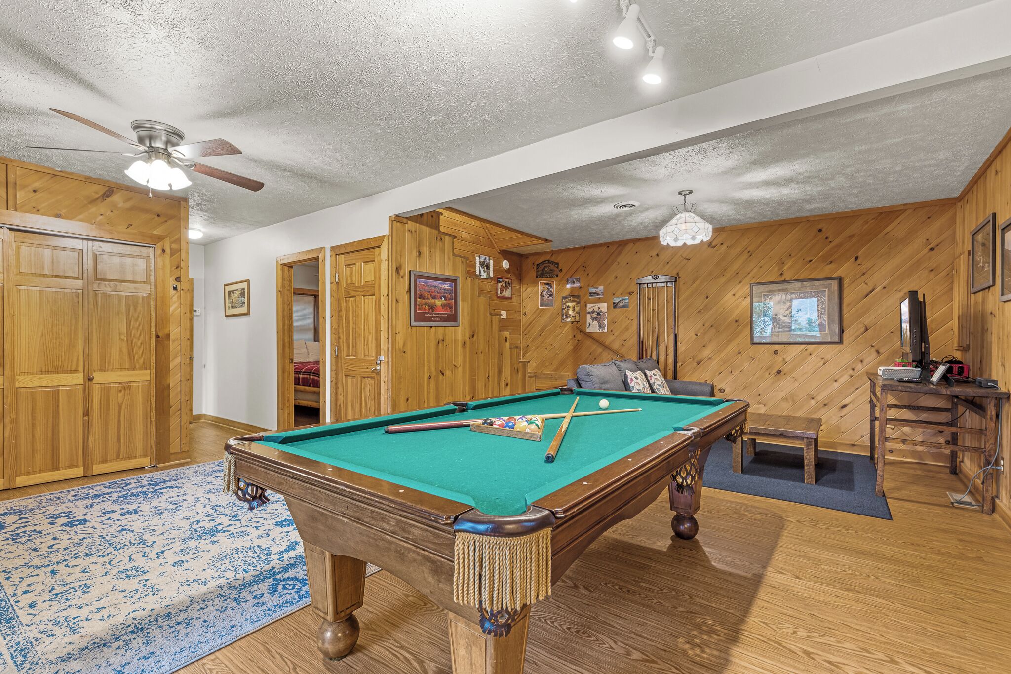 A pool table in a room with wooden walls and a ceiling fan.