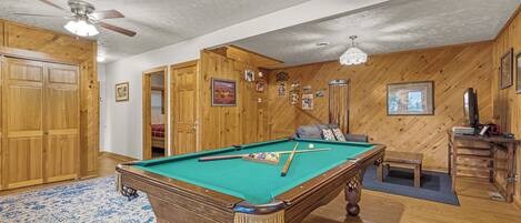 A pool table in a room with wooden walls and a ceiling fan.