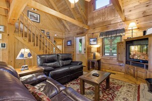 Interior de una cabaña de madera con un sofá de cuero, un televisor y una chimenea.