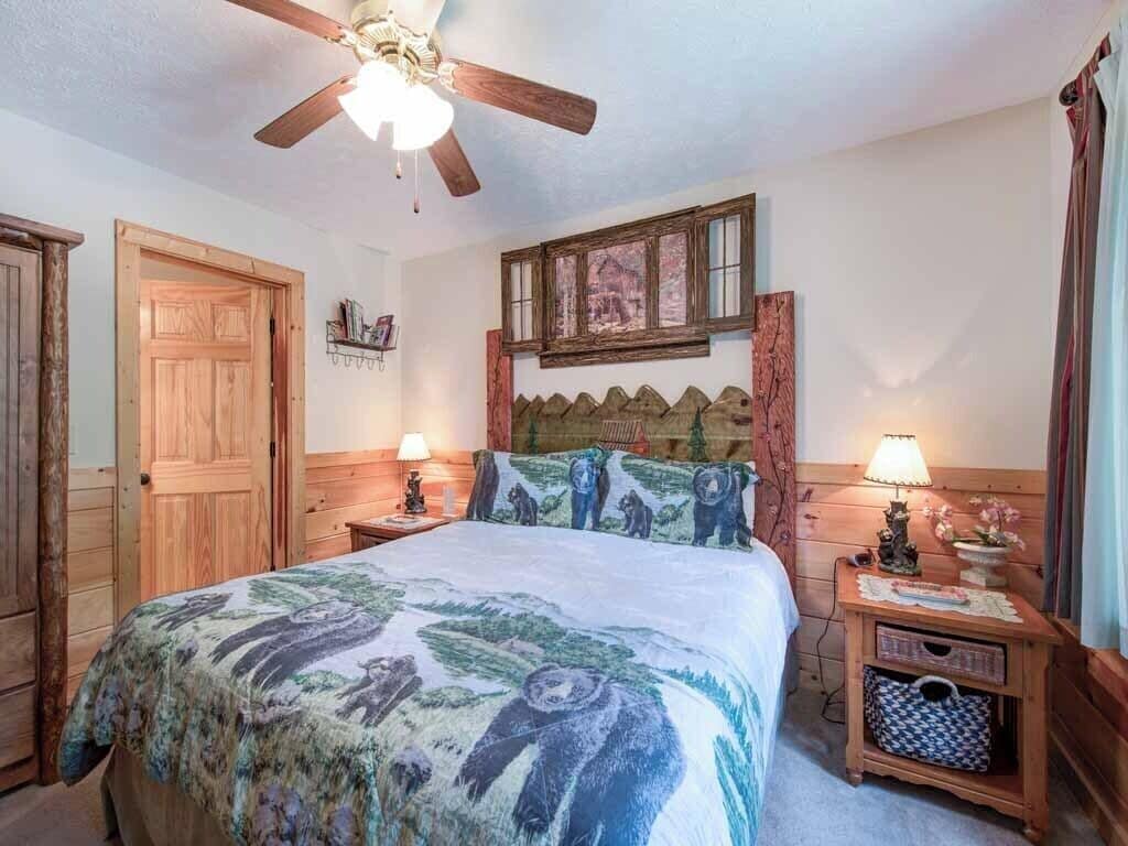 Un dormitorio con cama de madera, ventilador de techo, ventana con vistas y mesita de noche con lámpara.