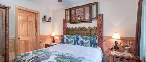 Un dormitorio con cama de madera, ventilador de techo, ventana con vistas y mesita de noche con lámpara.