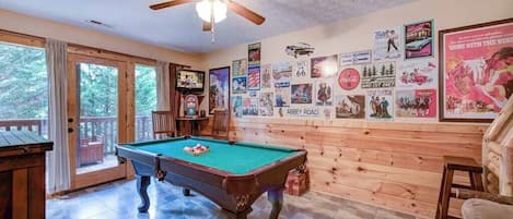 Sala com piscina, mesa de bilhar, paredes de madeira e diversos cartazes.