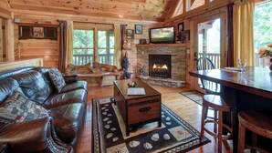 Un acogedor interior de cabaña con un sofá de cuero, una chimenea, una mesa de comedor y un ventilador de techo.