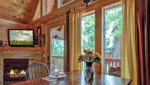 Una mesa de comedor de madera con una chimenea, un televisor montado encima y una ventana con cortinas.