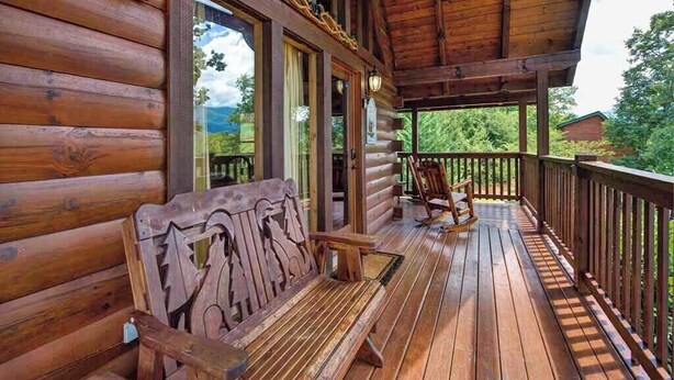 Una cabaña de madera con porche, bancos de madera y una mecedora.