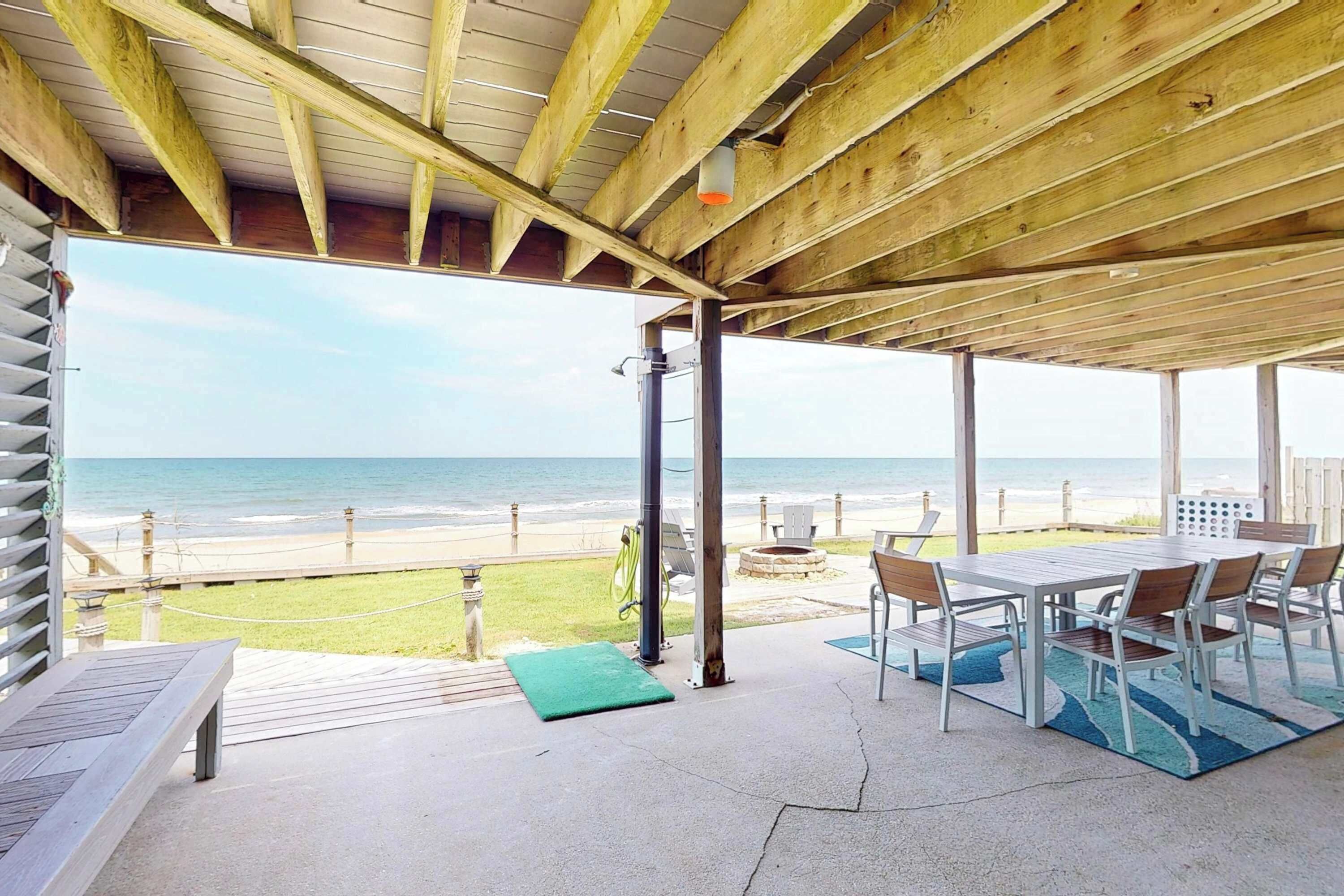 Une terrasse couverte avec vue sur la plage, du mobilier d’extérieur et une structure de plafond en bois.
