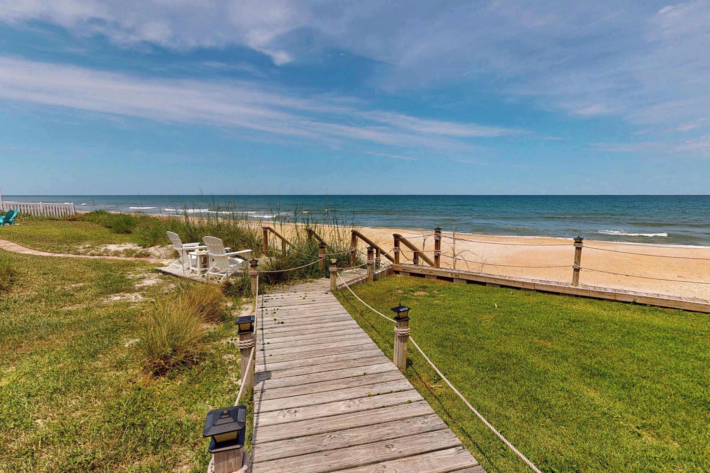 A wooden boardwalk leading to a beach with a fence and chairs.
