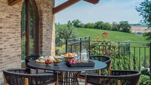 A round table with wicker chairs on a balcony with a brick wall and a view of a green field. - Villa Flavia - Private villa, 8 bedrooms, pool, A/C, wifi, pets, Marche (Filottrano)