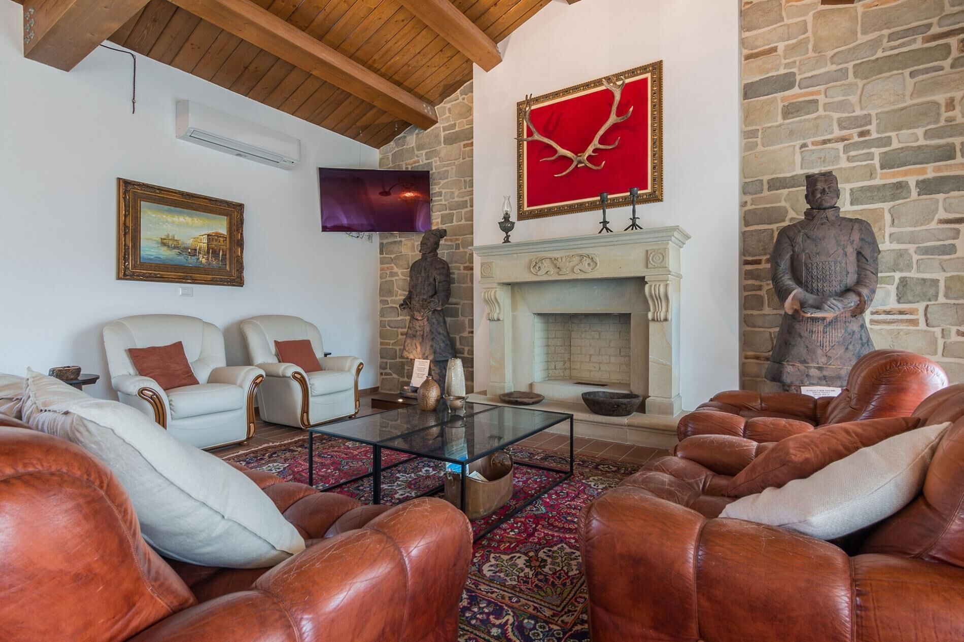 Una sala de estar con sofás de cuero, una mesa de centro de vidrio, una chimenea de piedra y un televisor montado.