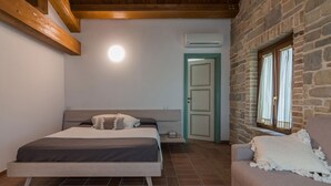 A bedroom with a bed, a nightstand, a stone wall, a window with curtains, and a wooden ceiling beam. - Villa Flavia - Private villa, 6 bedrooms, pool, A/C, wifi, pets, Marche (Filottrano)