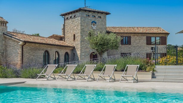 A pool area with lounge chairs and a stone building with a tower. - Villa Flavia - Private villa, 6 bedrooms, pool, A/C, wifi, pets, Marche (Filottrano)