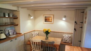 Tunnelmallinen keittiö, jossa on puiset kaapit, puinen ruokapöytä, kaksi tuolia, maljakko, jossa on keltaisia kukkia, ja seinällä oleva kehystetty kuva.