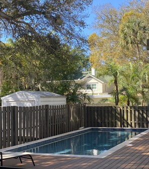 A swimming pool with a wooden deck, surrounded by a wooden fence and trees.