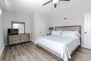 Une chambre à coucher comprenant un lit, une commode, un téléviseur, un ventilateur de plafond et une porte.