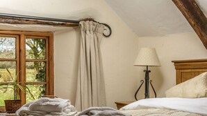 A bedroom with a bed, a bedside table, a lamp, a window with curtains, and a view of greenery outside.