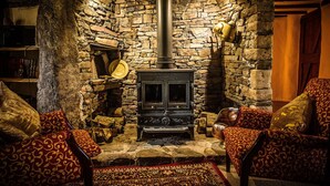 A cozy room with a stone fireplace, a wooden table, and patterned chairs.