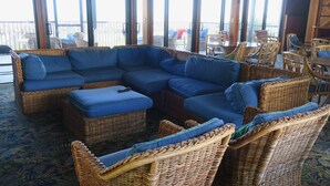 Un sofá seccional grande en forma de L con cojines azules en una habitación con ventanas amplias y muebles de mimbre.