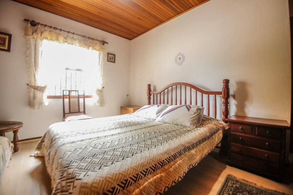 A bedroom with a wooden bed, a nightstand, a dresser, and a window with curtains.