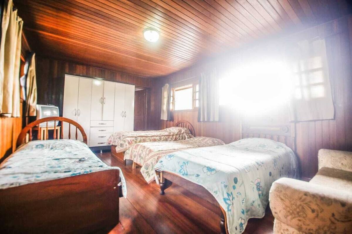 A room with wooden floors, two single beds with floral bedspreads, a wooden wardrobe, and a small table.