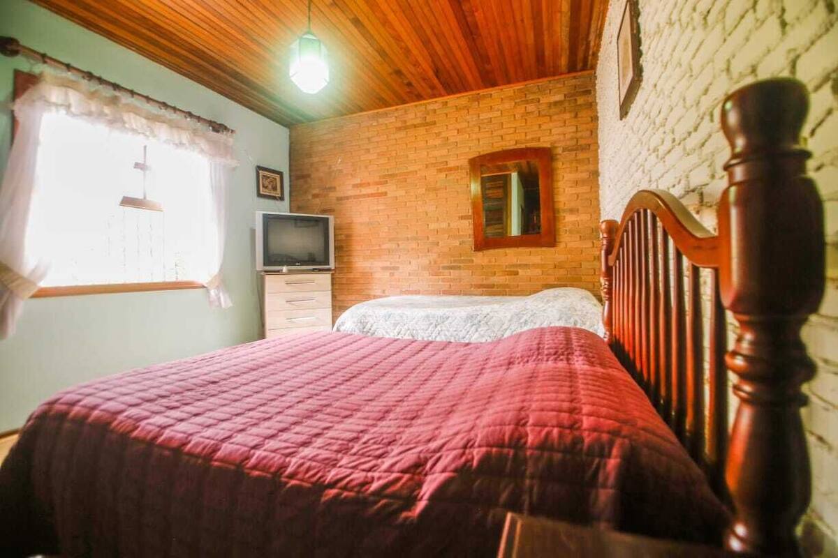 A bedroom with a wooden headboard, a brick wall, a television, and a window with curtains.