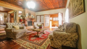 Un salon chaleureux avec une cheminée, deux fauteuils, un canapé et un tapis rouge à motifs.