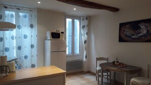 Una pequeña cocina equipada con microondas, refrigerador, una mesa de comedor con sillas y una ventana con cortinas.