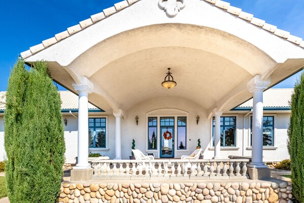 A covered porch with white columns, a stone base, and a central light fixture.