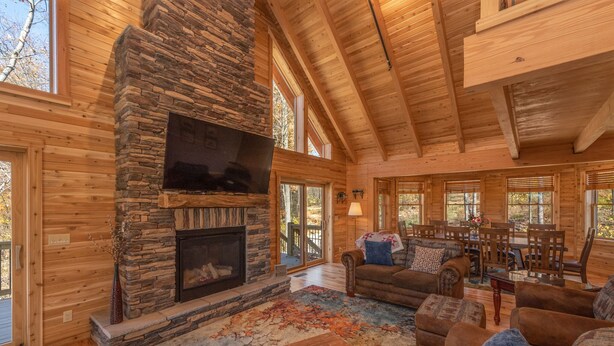 Un intérieur de chalet chaleureux avec une cheminée en pierre, des murs en bois et de grandes fenêtres.