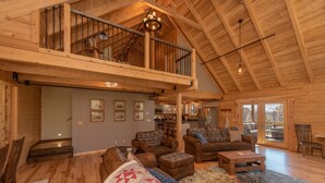 Un vaste espace de vie de style loft, doté d’un plafond haut, de poutres en bois, d’un escalier menant à un niveau supérieur et d’un coin salon confortable.