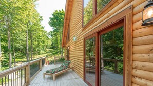 Une terrasse en bois avec un banc et des portes vitrées donnant sur une zone boisée.