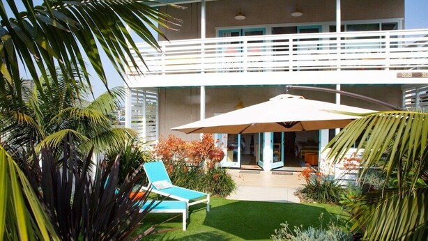 A two-story building with a balcony, a covered patio area, and a lawn with a lounge chair.