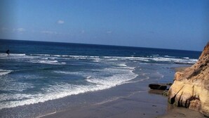 A beach with waves, a cliff, and a person in the distance.