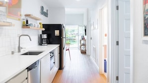 A modern kitchen with white cabinetry, a black refrigerator, and a coffee maker. There is a window providing natural light and a view of the outdoors.