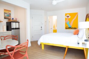 A bedroom with a bed, a desk, a chair, a refrigerator, and a wall with a poster.