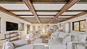 Ein geräumiger Wohnbereich mit einem großen weißen Sofa, einem Holztisch und einem Fernseher auf einem Holzgestell.