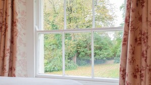 Una habitación con un ventanal grande, cortinas con motivos florales y vistas a árboles y vegetación.