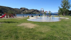 Une aire de jeux avec des toboggans et des balançoires, située près d’un lac.
