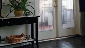 Une pièce avec un plancher en bois foncé, une petite table avec une lampe et une plante, un téléviseur fixé au mur et une porte dotée de panneaux en verre dépoli.