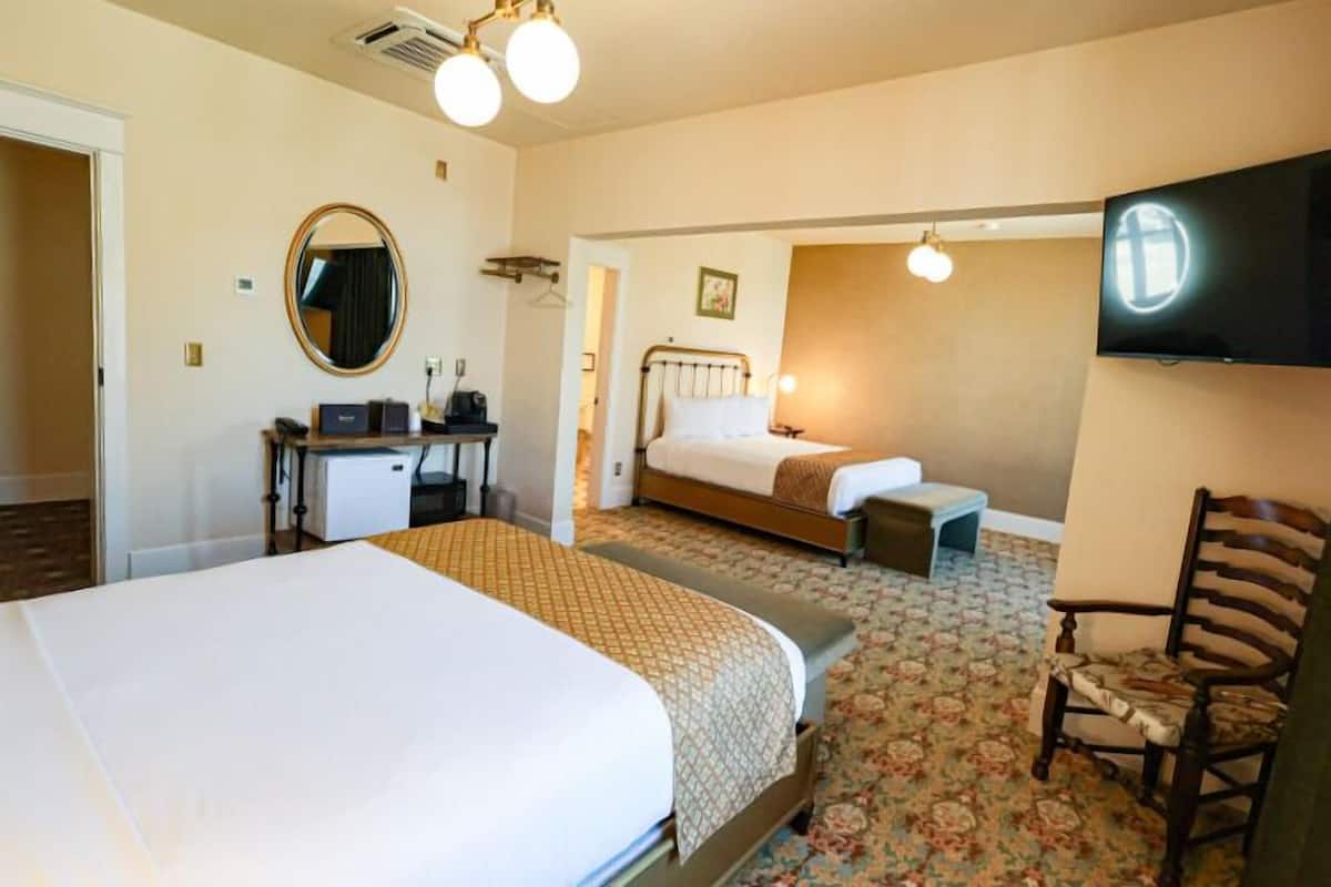 A hotel room with a large bed, a smaller bed, a desk with a computer, a chair, and a television on the wall.