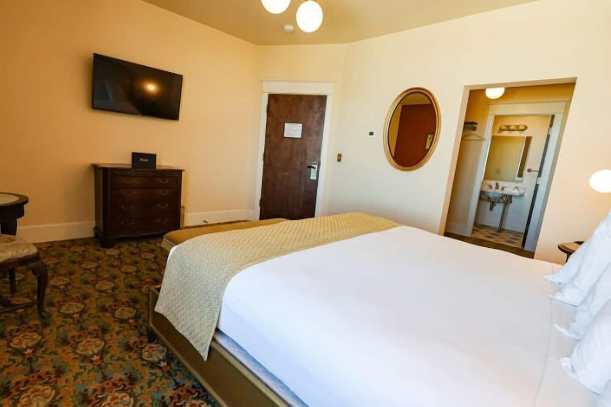 A hotel room with a bed, a dresser, a desk, a chair, a television, and a door.
