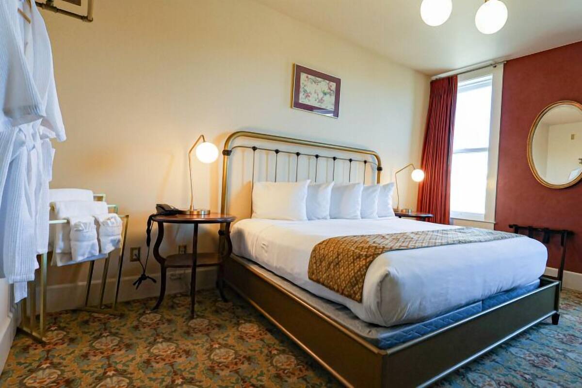 A hotel room with a bed, bedside lamps, a telephone, a mirror, and a floral carpet.